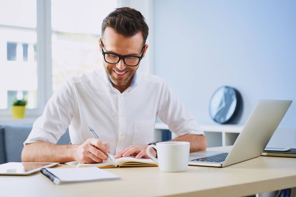 man writingatdesk infrontlaptop